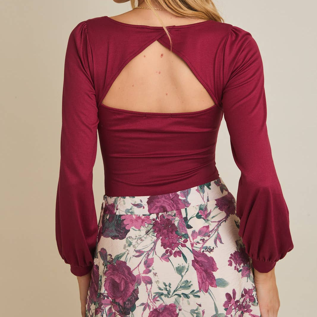Woman wearing a burgundy top with open back and floral skirt on a beige background