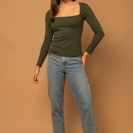 Woman wearing a green long-sleeve top and blue jeans against a brown background