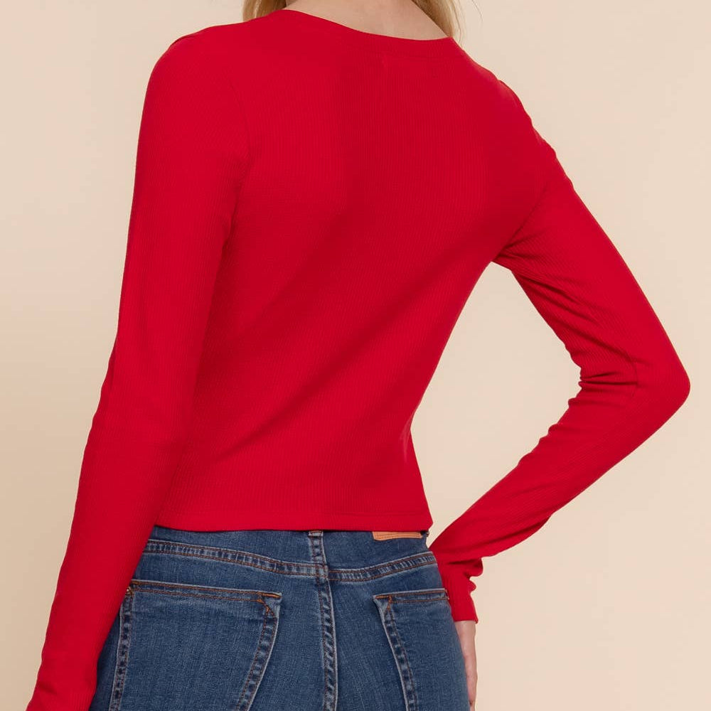 Woman wearing a red long-sleeve top and blue jeans on a beige background