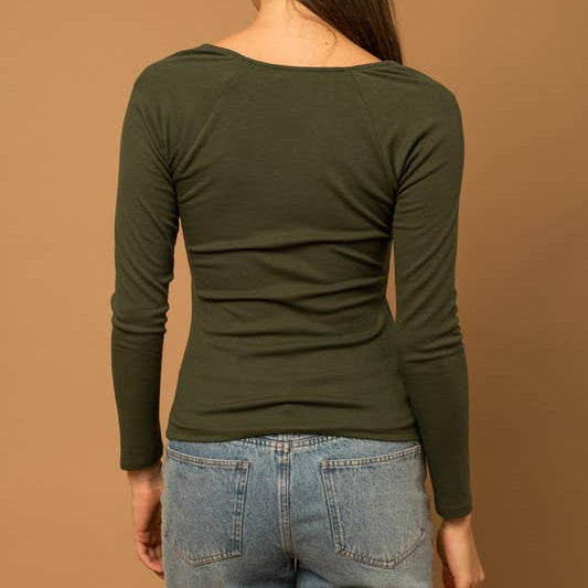 Person wearing a green long-sleeve top and blue jeans against a brown background