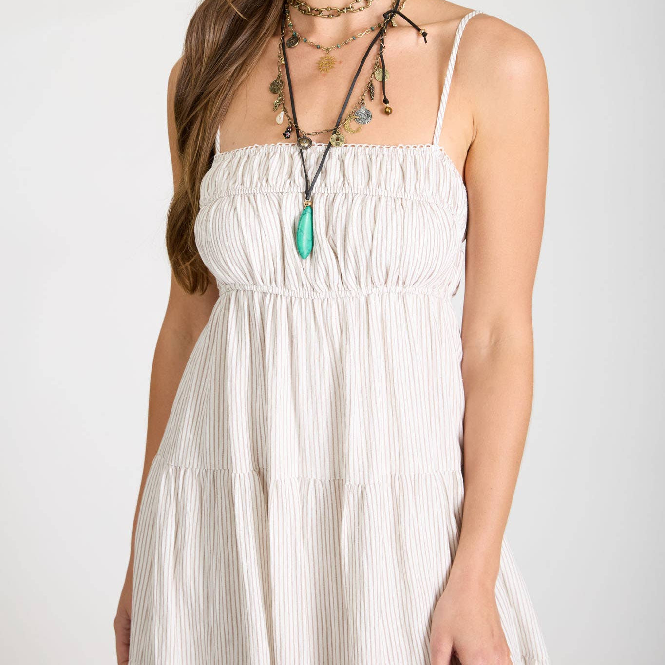 Woman wearing a white dress with layered necklaces on a plain background