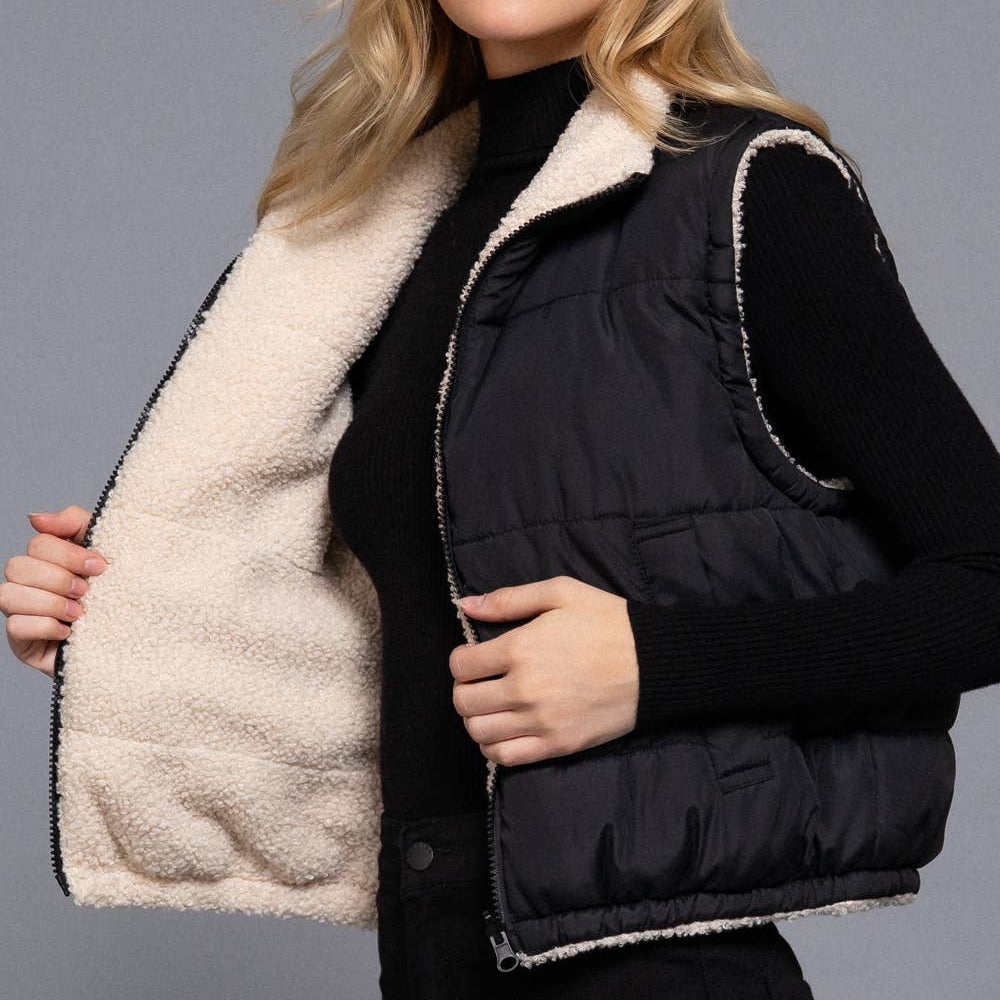 Woman wearing a black puffer vest with beige interior on a gray background