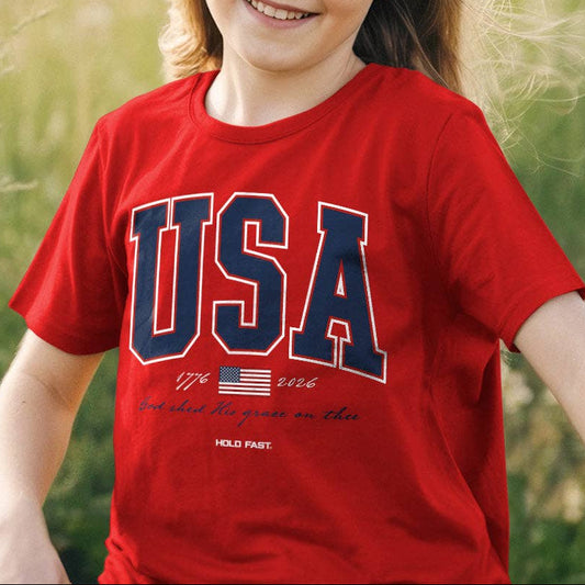Young girl wearing a red 'USA' t-shirt in a grassy field