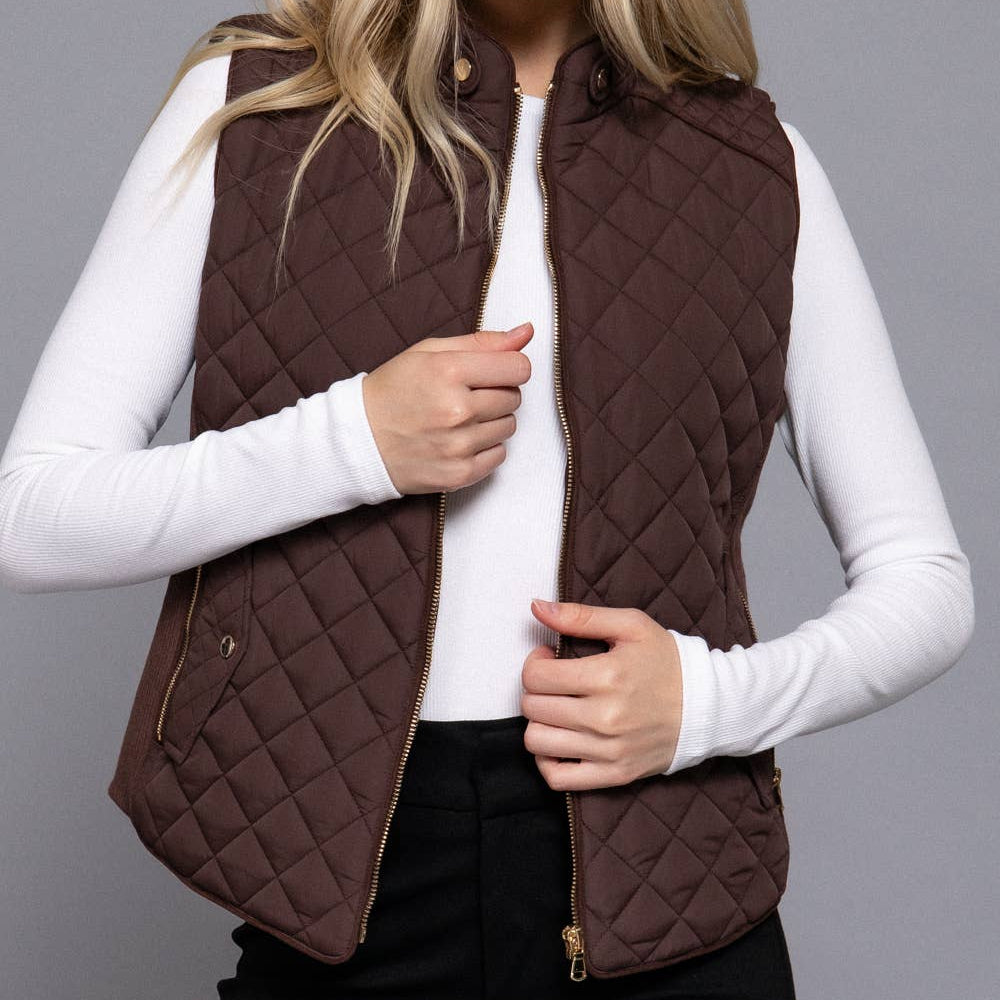 Woman wearing a brown quilted vest over a white long-sleeve shirt on a gray background