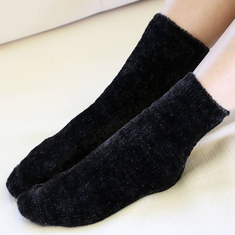 A pair of black fuzzy ankle socks worn on feet, shown against a light cream-colored background.