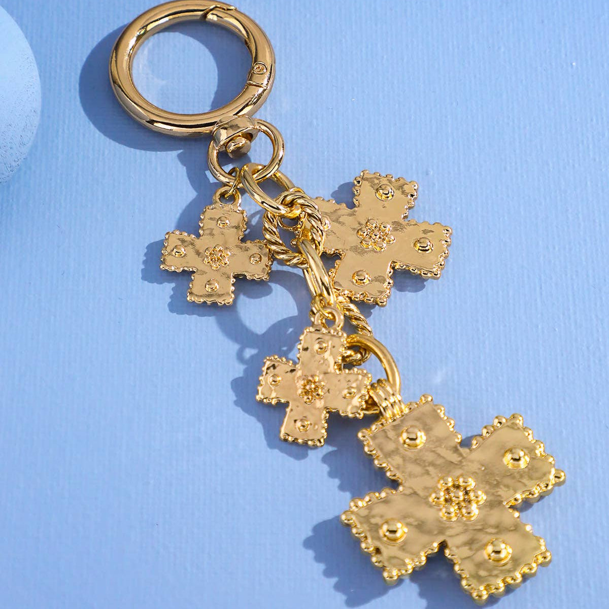 A gold-tone metal keychain featuring three textured cross charms of varying sizes attached to a split ring, displayed on a light blue background.