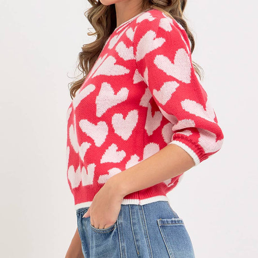 Woman wearing a red sweater with white heart patterns and blue jeans on a light gray background