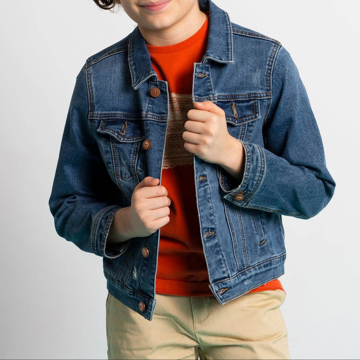 Child wearing a denim jacket over an orange shirt on a plain background