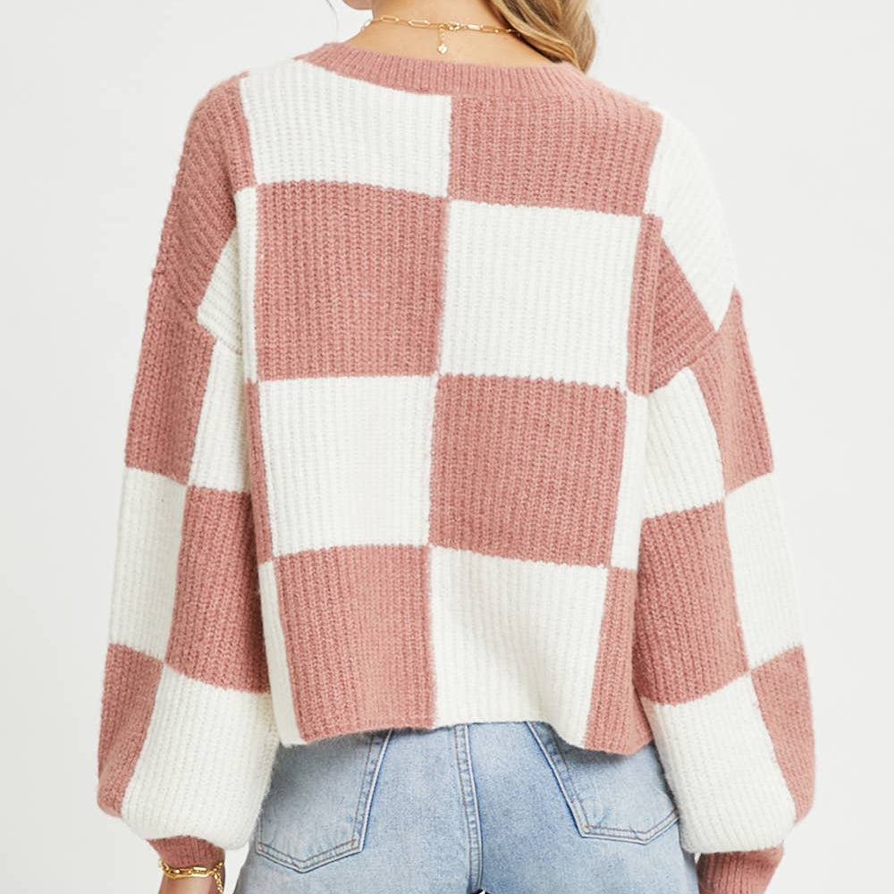 Person wearing a checkered sweater with pink and white pattern on a plain background