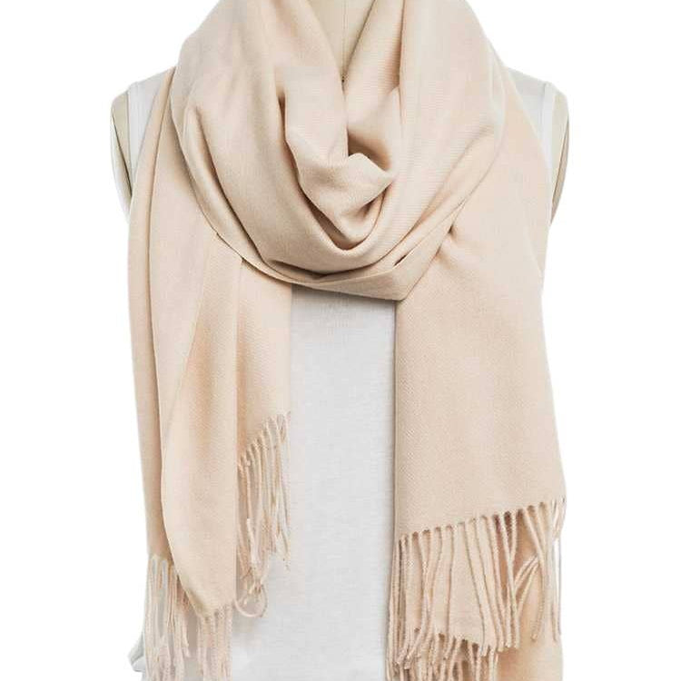 A light beige fringed scarf wrapped around a mannequin torso wearing a white top and blue jeans against a plain white background.