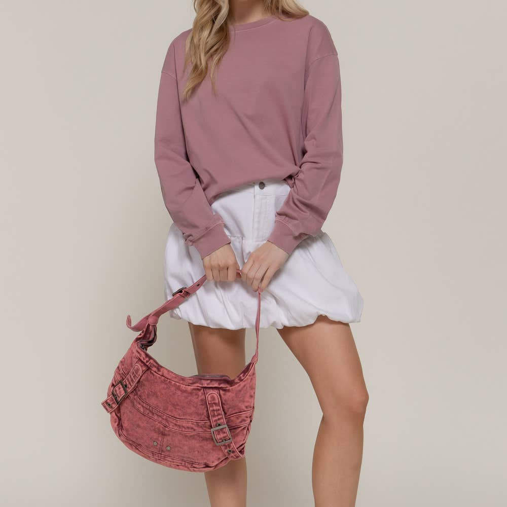 Woman wearing a pink sweater and white shorts, holding a red bag against a beige background