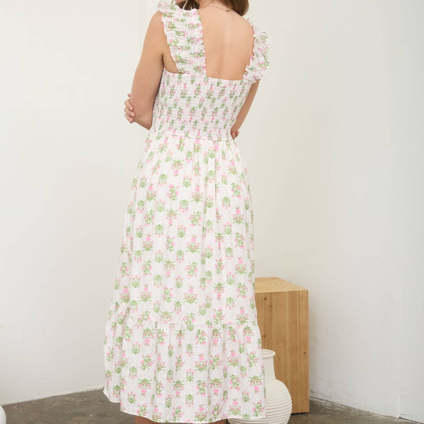 Woman wearing a floral dress standing against a white wall.