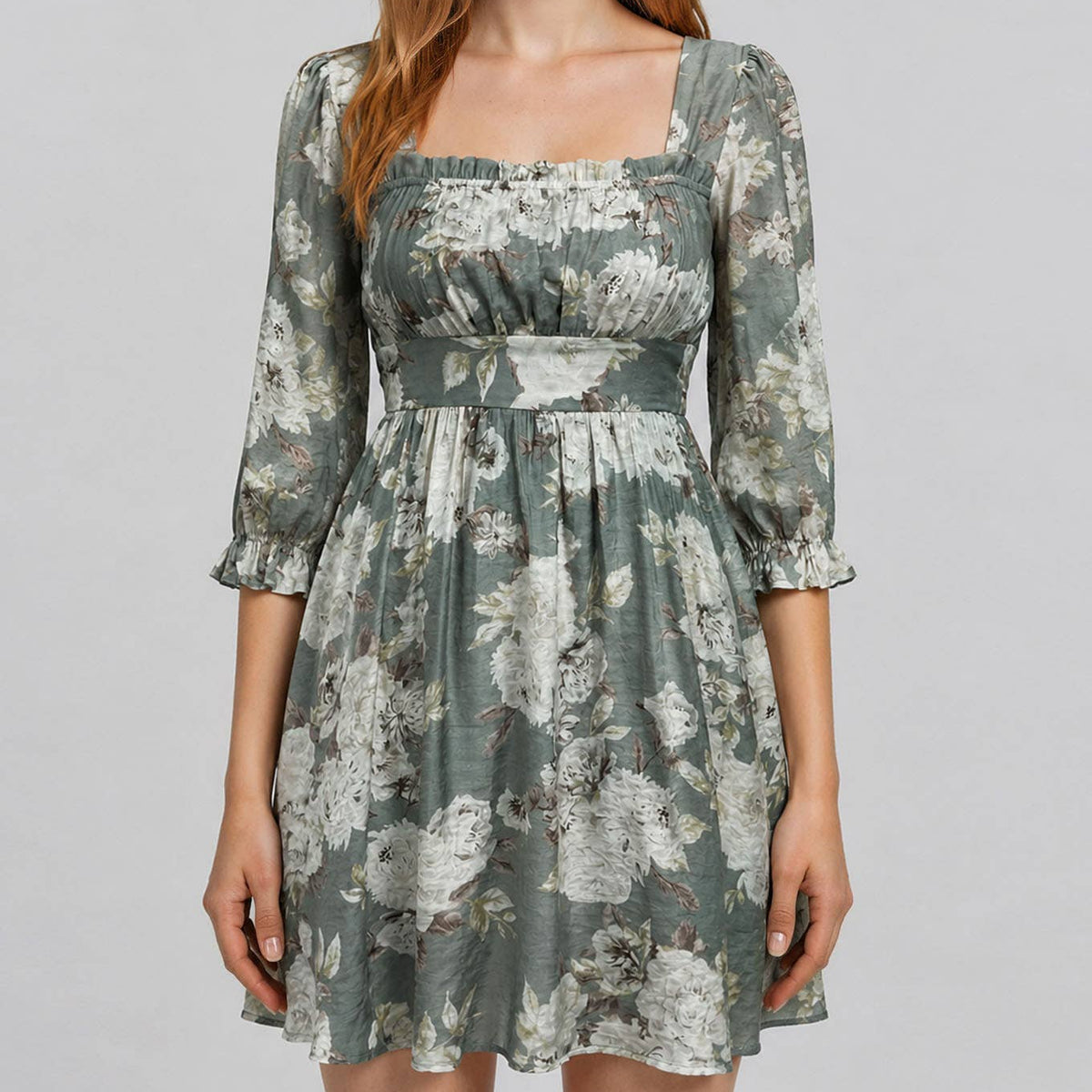 A woman modeling a short floral dress with a square neckline, three-quarter sleeves, and a gathered waist, shown against a plain light gray studio background.