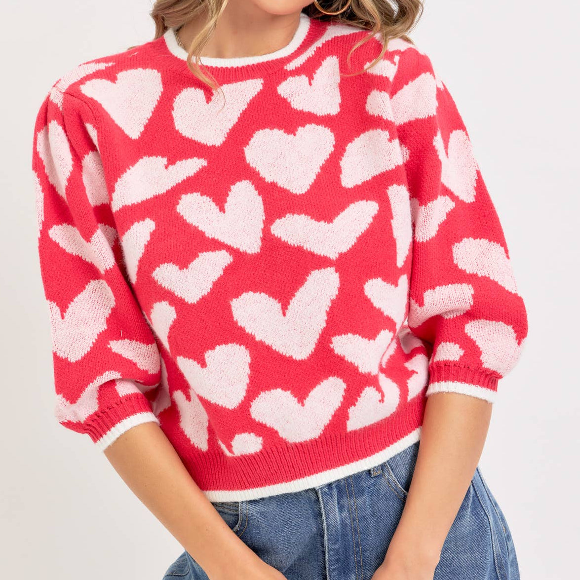 Woman wearing a red sweater with white heart patterns on a plain background
