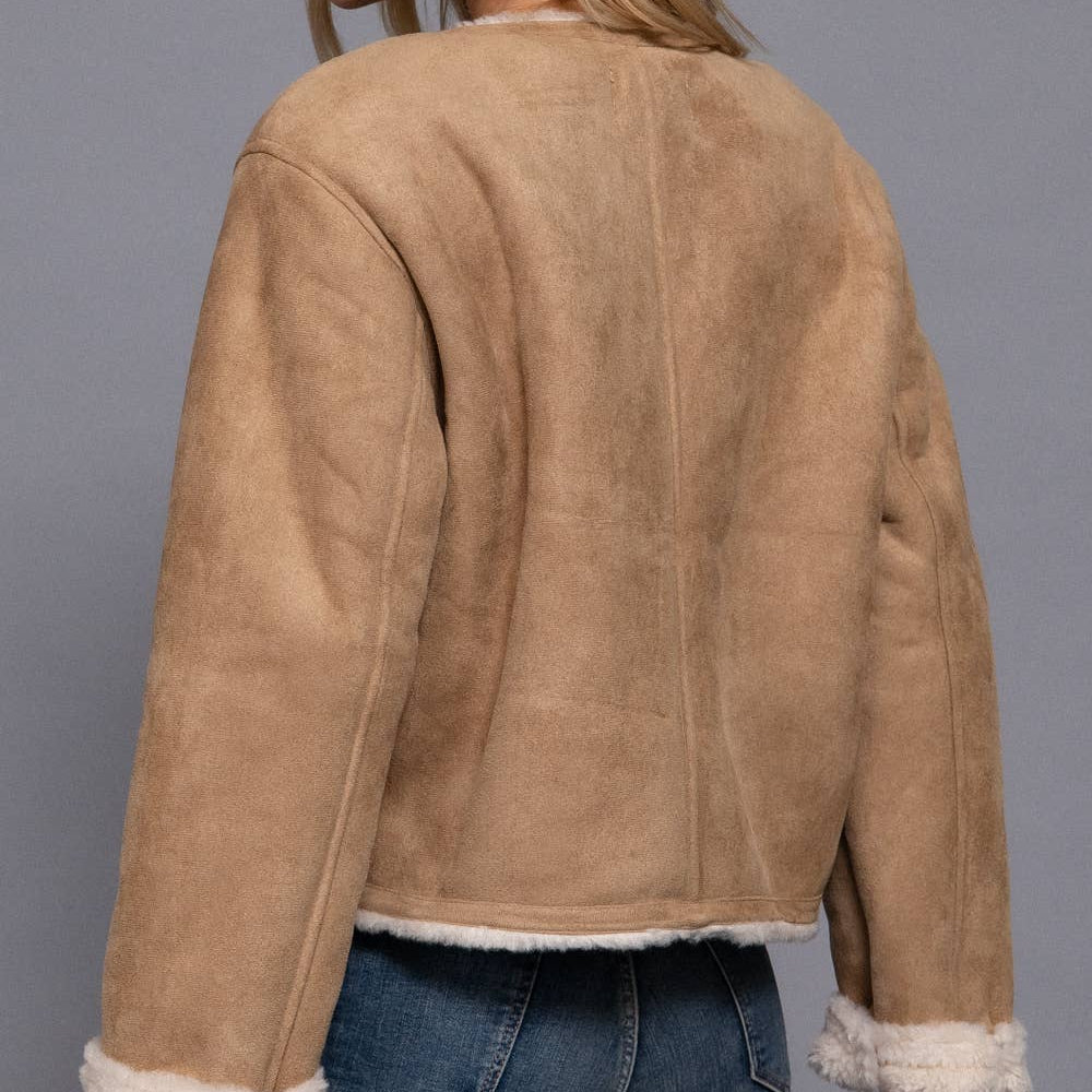 Woman wearing a tan suede jacket with white trim on a gray background