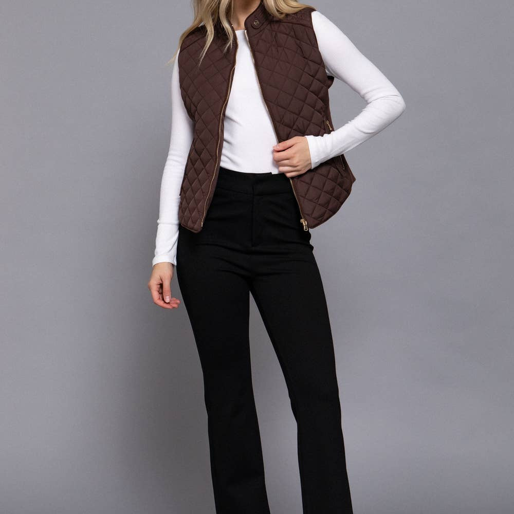 Woman wearing a brown quilted vest over a white long-sleeve shirt with black pants on a gray background