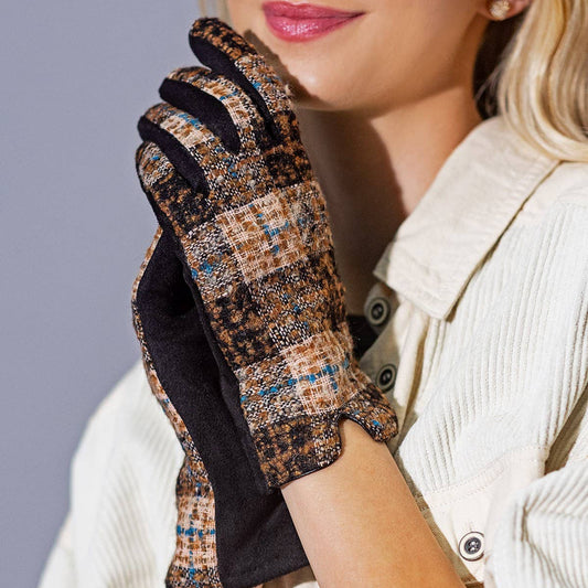 A blonde woman wearing a cream-colored corduroy jacket and holding up a pair of plaid tweed touchscreen gloves with black palms, posing against a solid gray studio background.