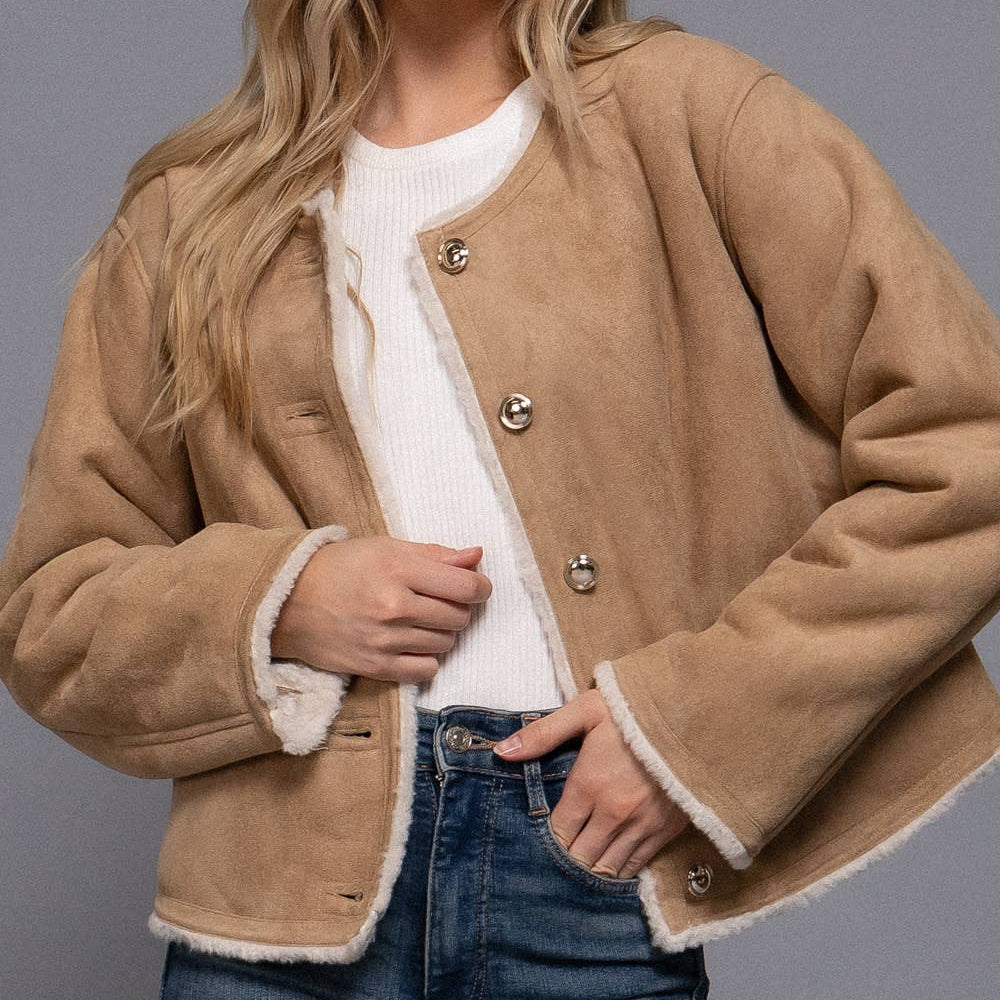 Woman wearing a beige shearling jacket with white trim on a gray background