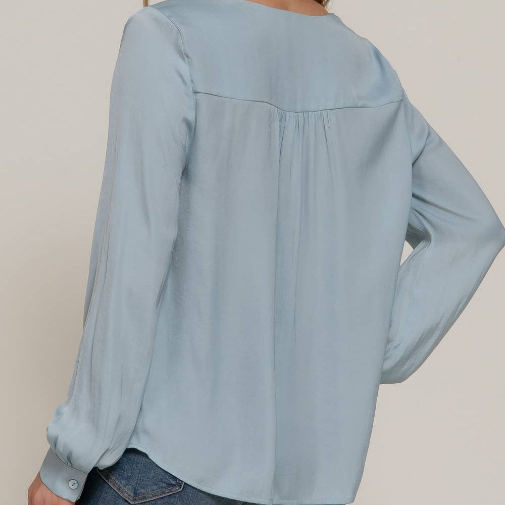 Woman wearing a light blue blouse with long sleeves against a plain background