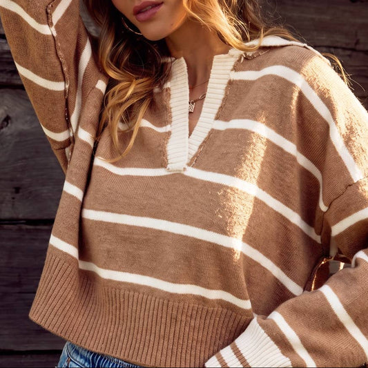 A woman wearing a brown and cream striped knit sweater with a split V-neck, posing against a rustic dark wood plank wall.