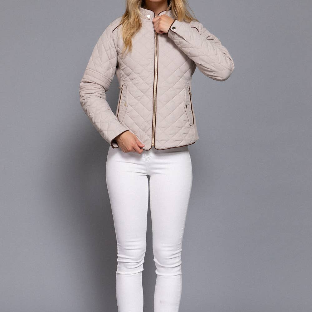 Woman wearing a beige quilted jacket and white pants on a gray background