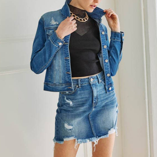 Woman wearing a denim jacket and skirt indoors with a neutral background