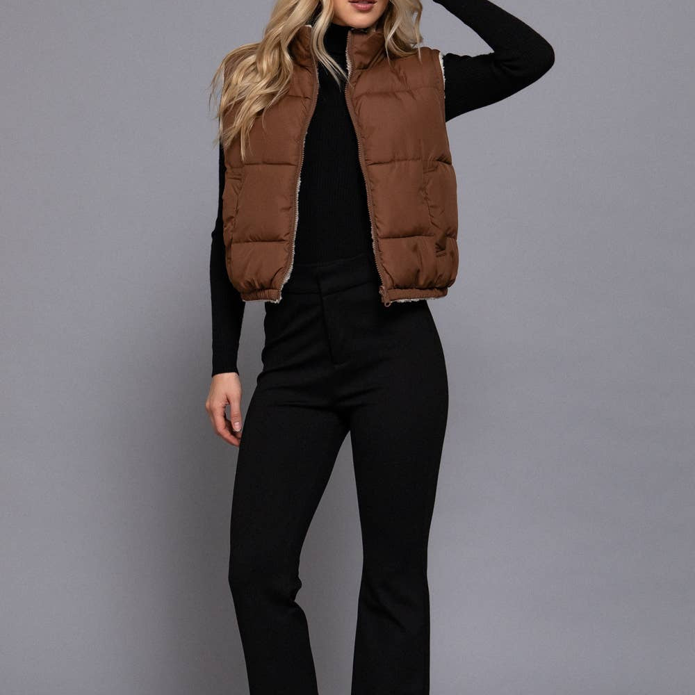 Woman wearing a brown puffer vest over a black top and pants on a gray background