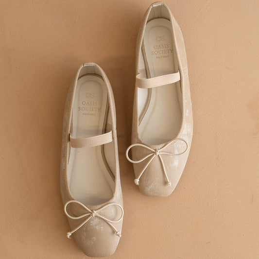 Pair of beige ballet flats with bow details on a beige background
