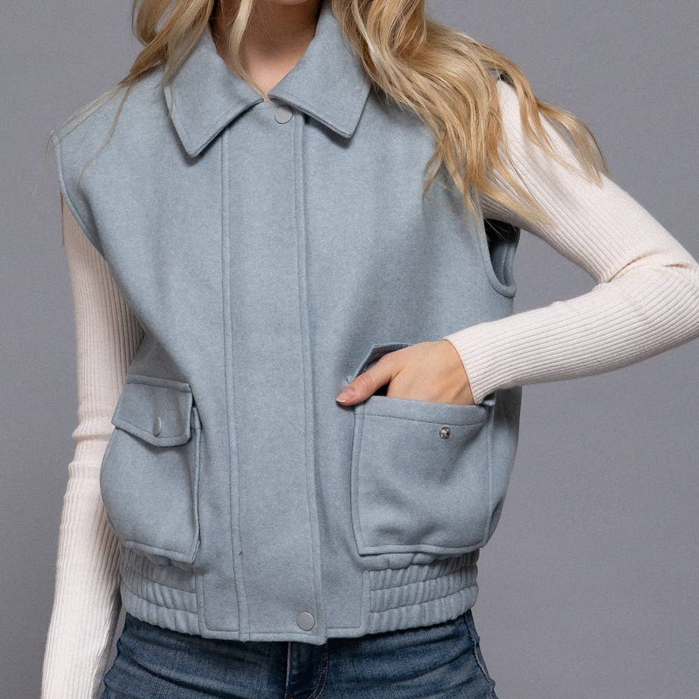 Woman wearing a light blue vest over a white long-sleeve shirt on a gray background