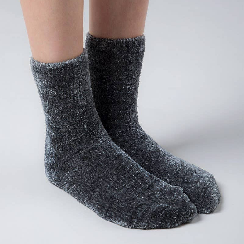 A pair of dark gray heathered knit crew socks worn on a person's feet, shown against a neutral light gray studio background.