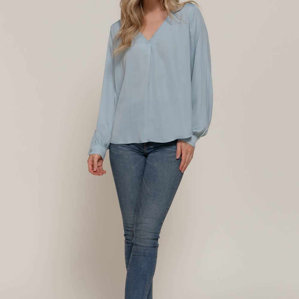 Woman wearing a light blue blouse and jeans against a plain background