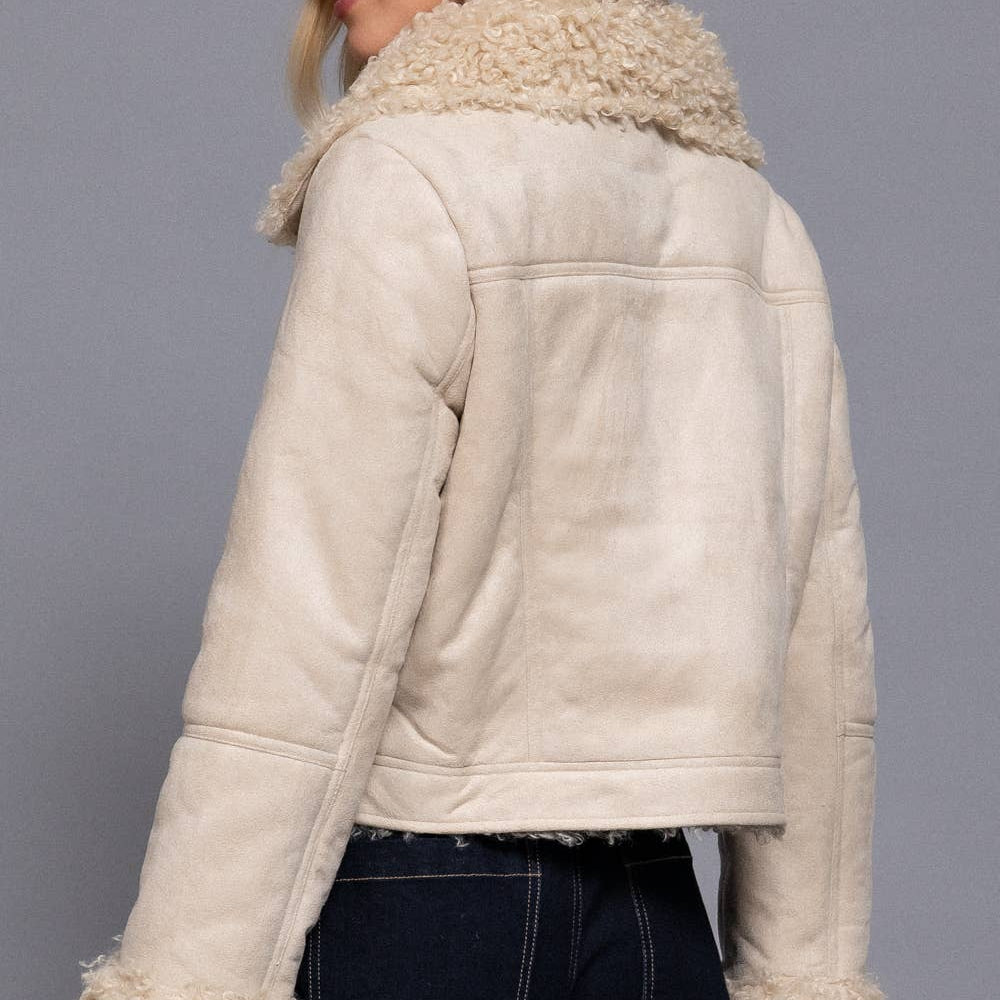 Woman wearing a cream-colored shearling jacket against a gray background