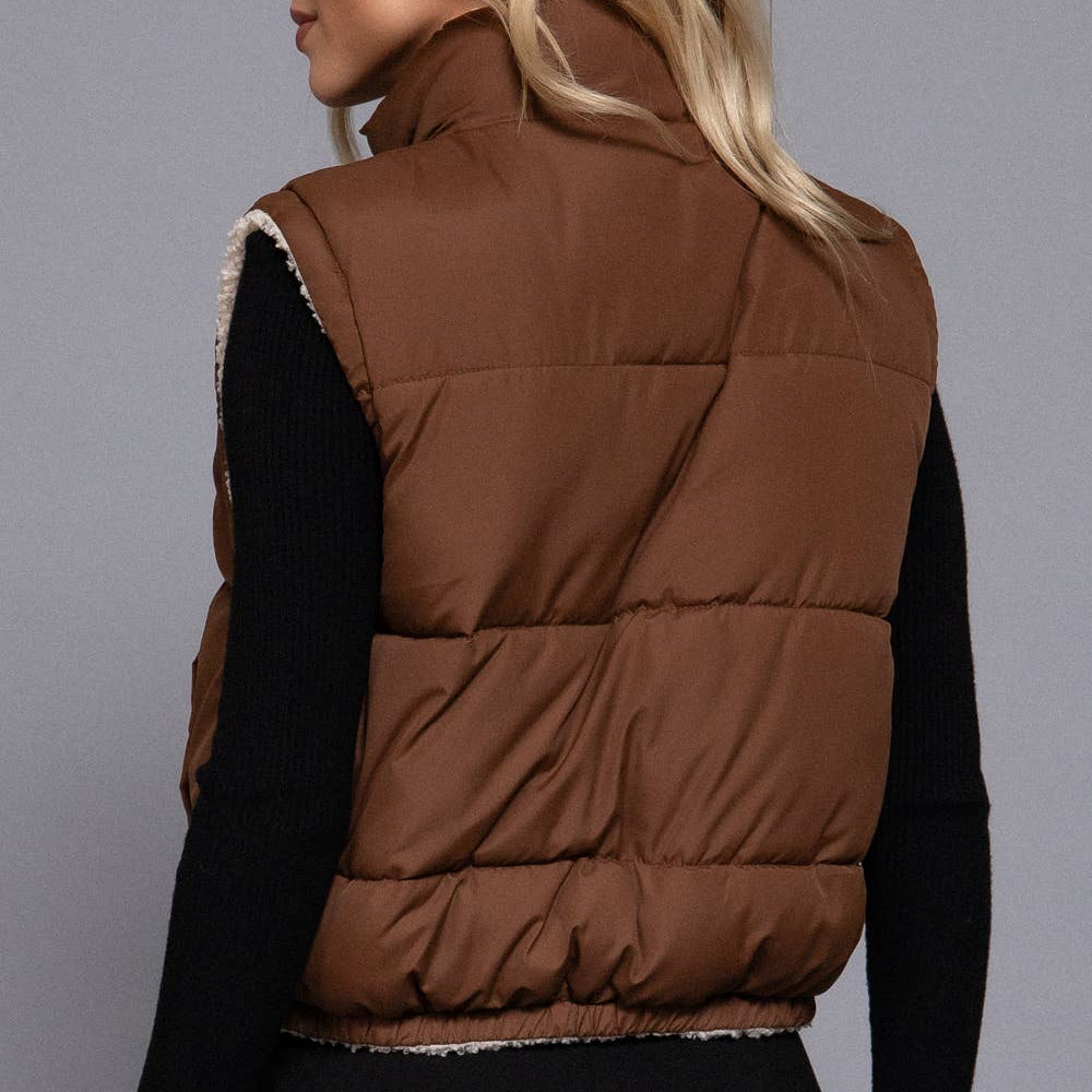 Woman wearing a brown puffer vest against a gray background