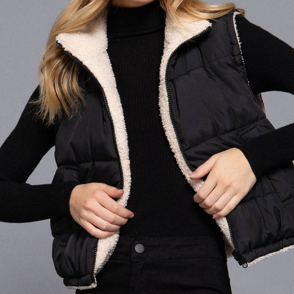 Woman wearing a black puffer vest with beige interior against a gray background