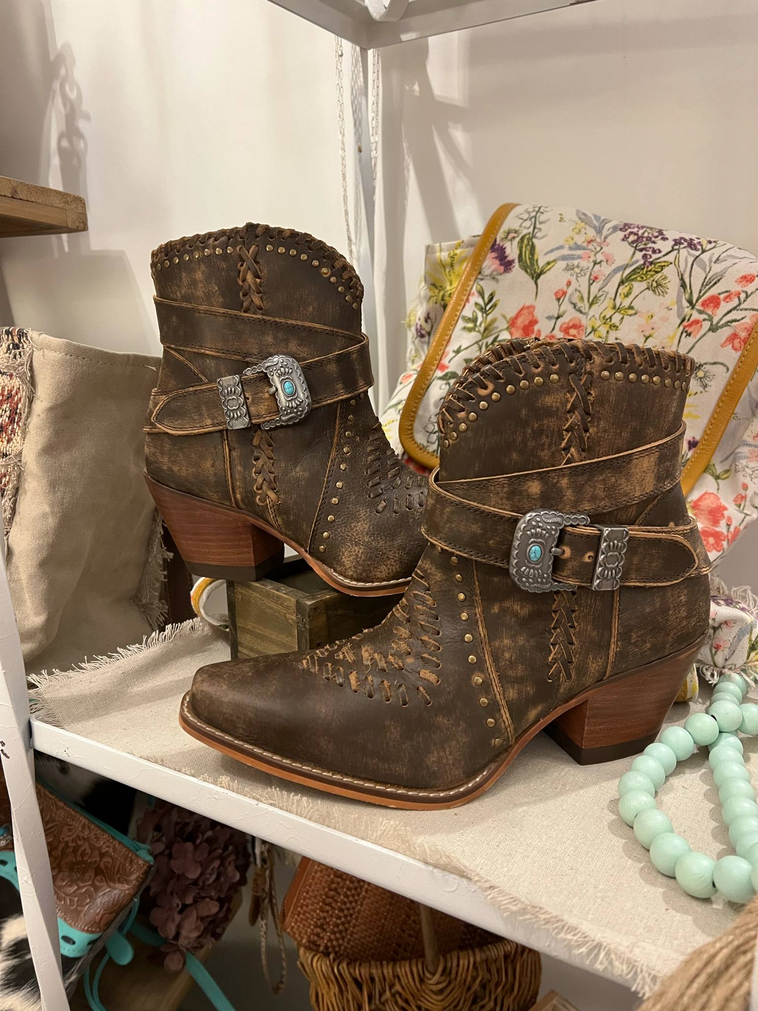 Pair of brown leather boots with decorative buckles on a white shelf.