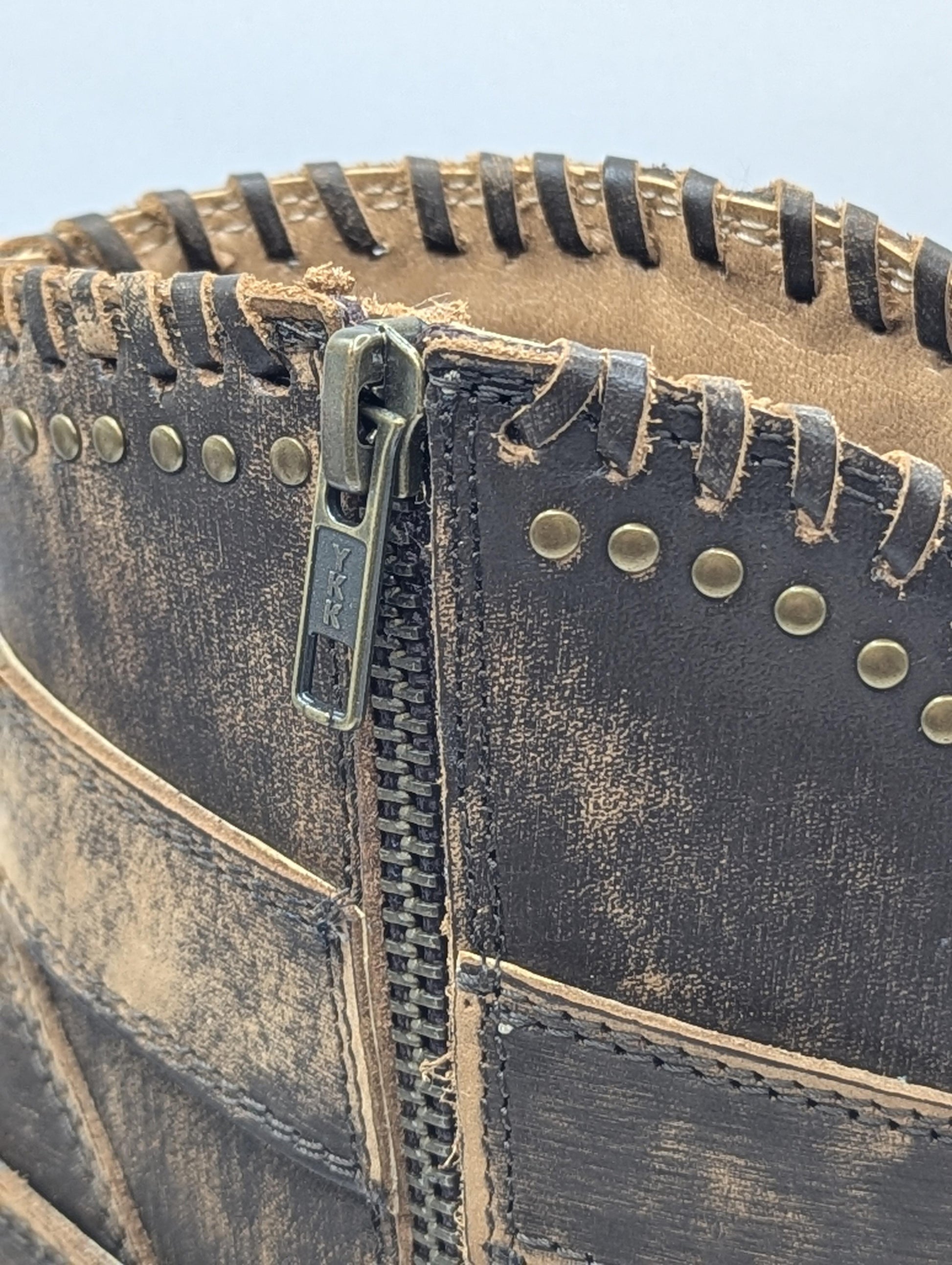 Close-up of a leather product with a zipper and metal studs on a white background